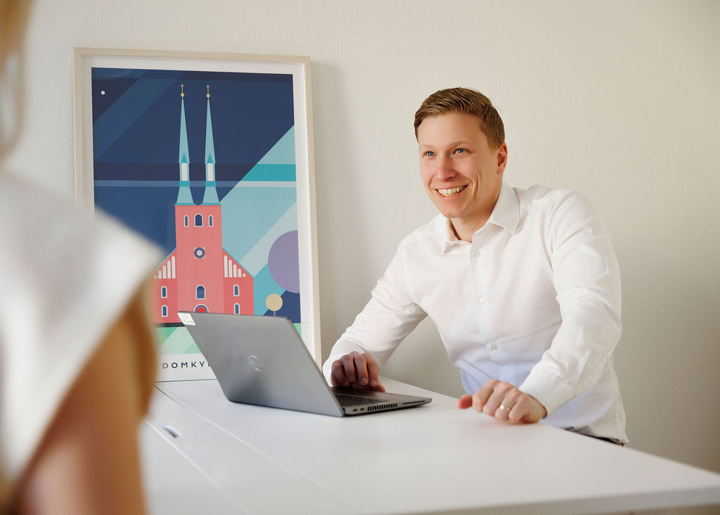 Rickard sitter vid sin laptop och ler mot en kollega